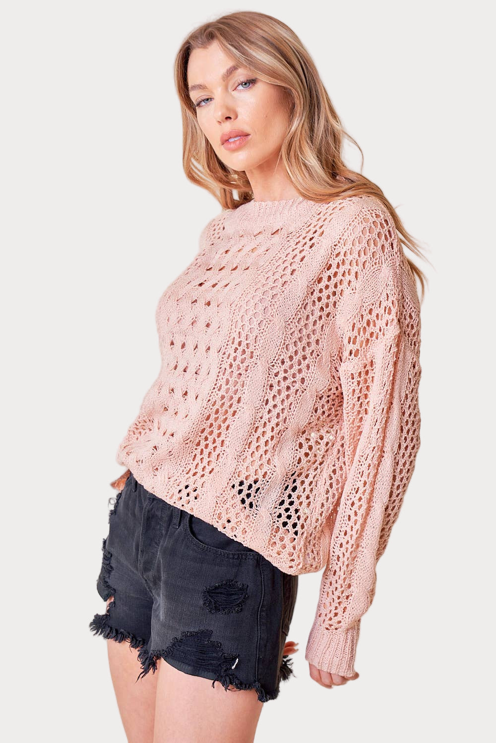 Woman wearing a pink knit sweater and black shorts on a white background