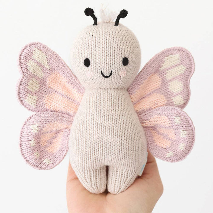 Knitted butterfly toy held in a hand against a white background