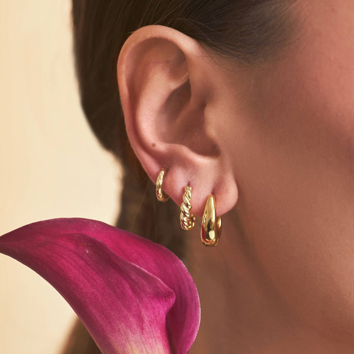 Close-up of a person wearing gold hoop earrings with a pink flower in the foreground.
