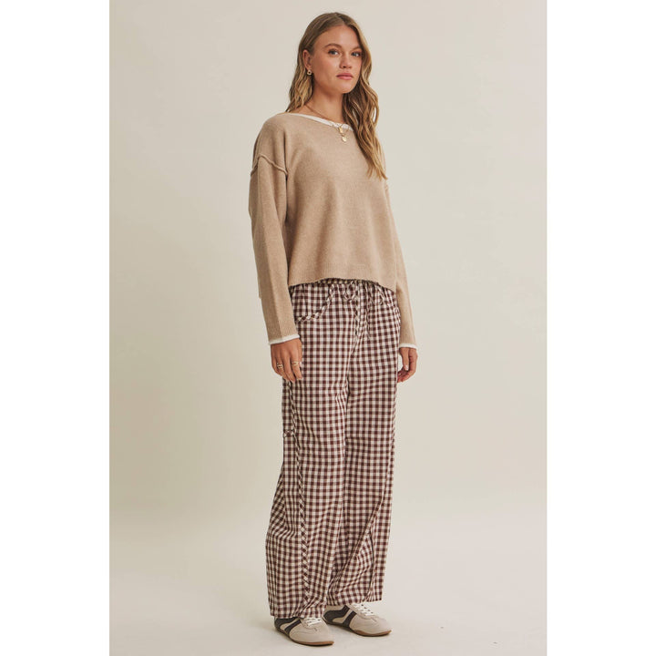 Woman wearing a beige sweater and checkered pants on a plain background