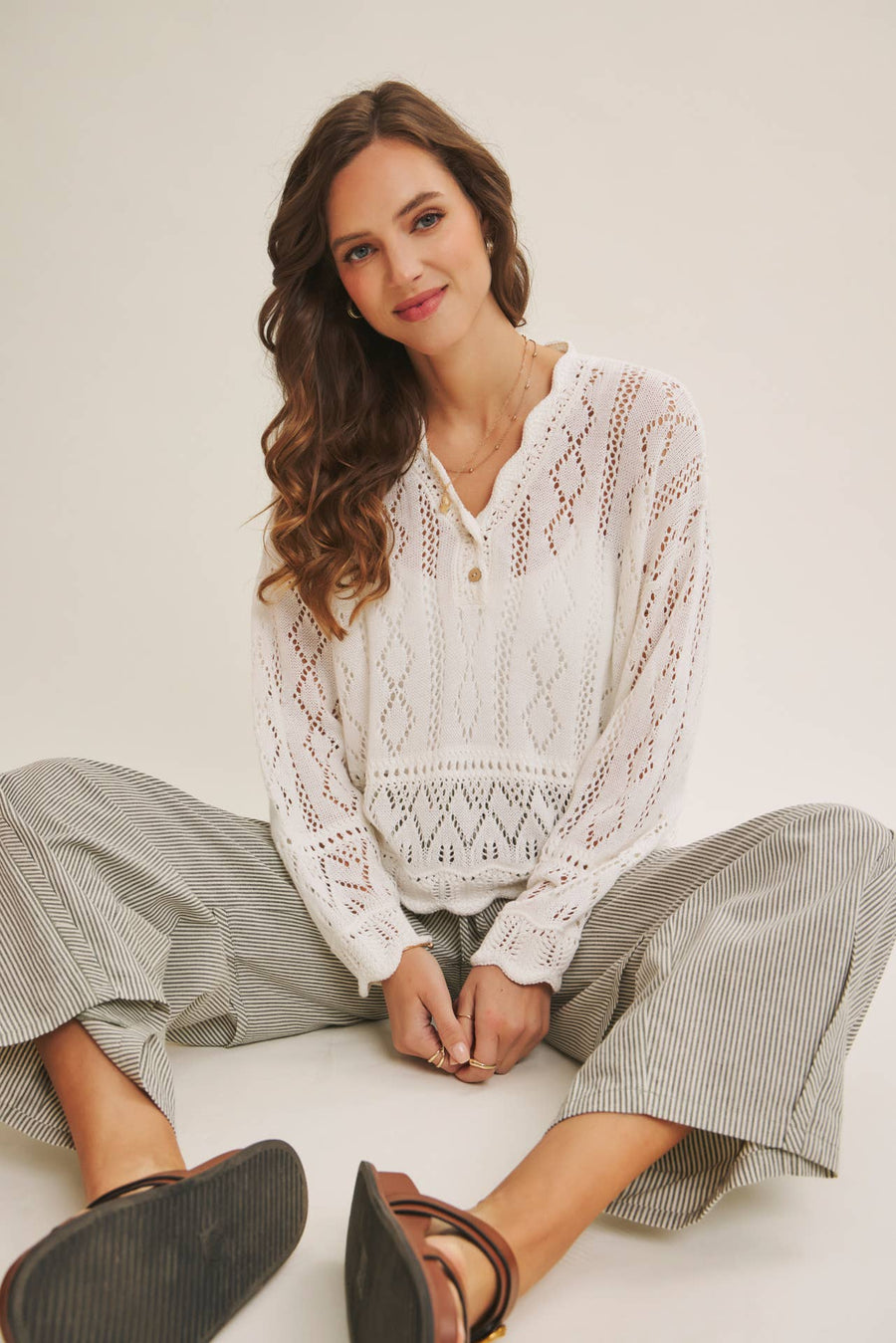 Woman wearing a white open-knit crochet sweater top with scalloped hem and long sleeves