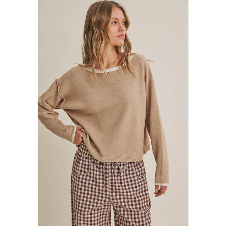 Woman wearing a beige sweater and checkered pants against a neutral background