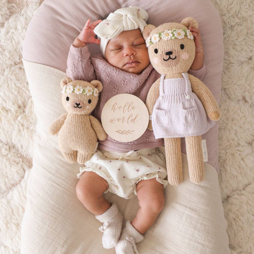 Newborn baby with two teddy bears and a 'hello world' sign on a soft surface