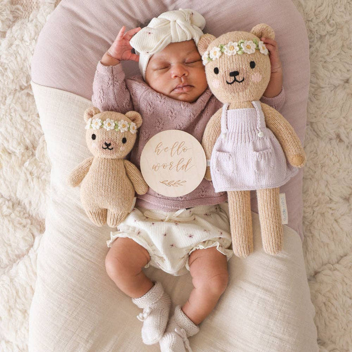 Newborn baby with two teddy bears and a 'hello world' sign on a soft surface
