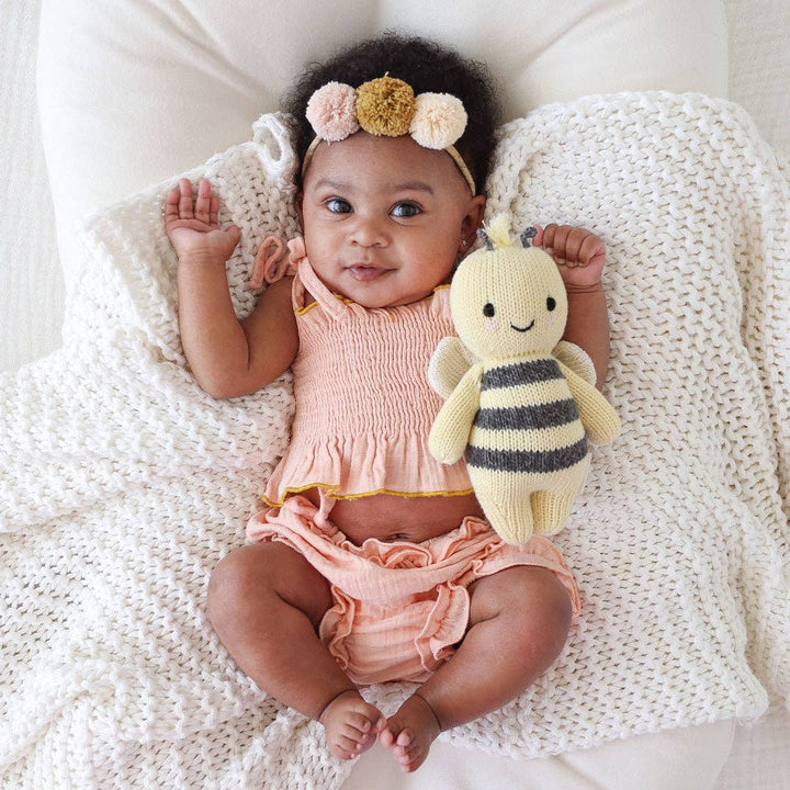 Baby girl in pink outfit holding a bee plush toy on a white blanket