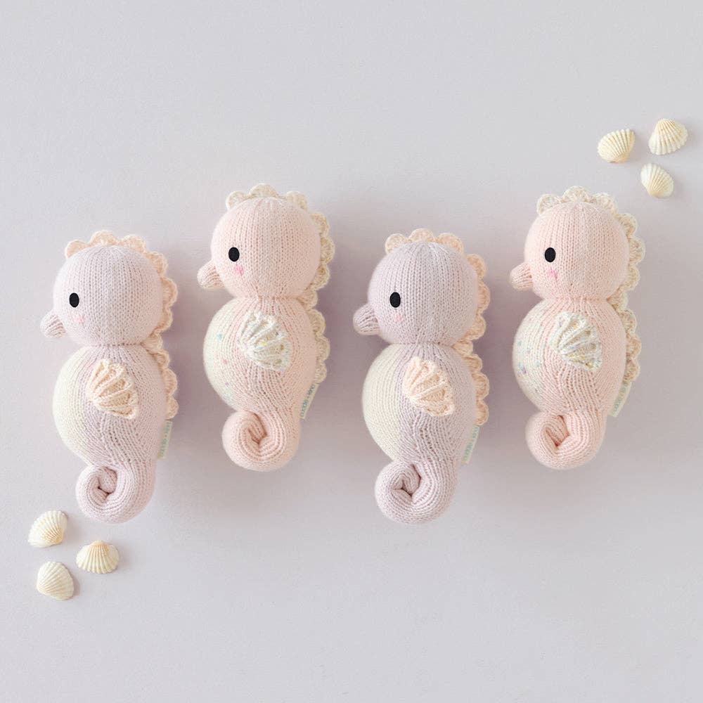 Four knitted seahorse toys on a light gray background with small shells.