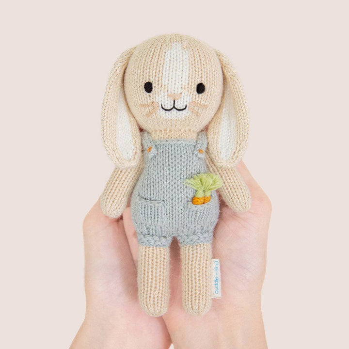 Knitted toy rabbit held in a hand with a plain background