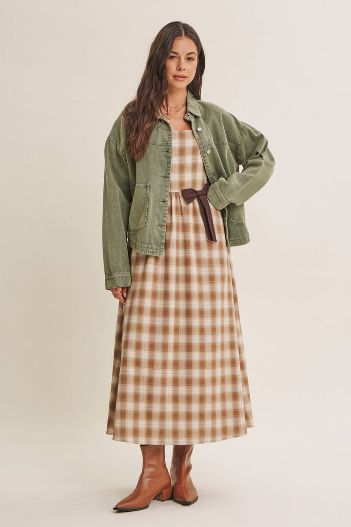 Woman wearing a olive green jacket over a plaid dress on a beige background