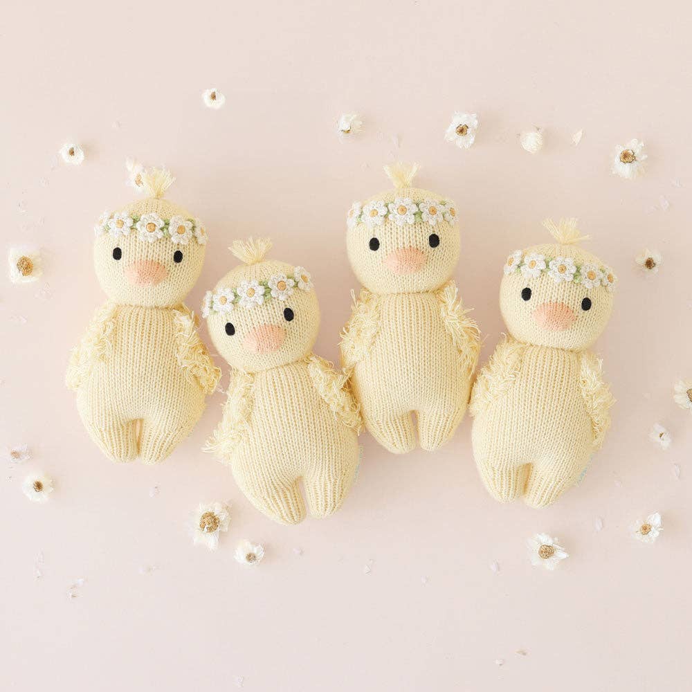 Four knitted baby ducks with floral crowns on a light pink background