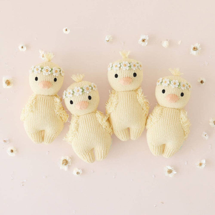 Four knitted baby ducks with floral crowns on a light pink background