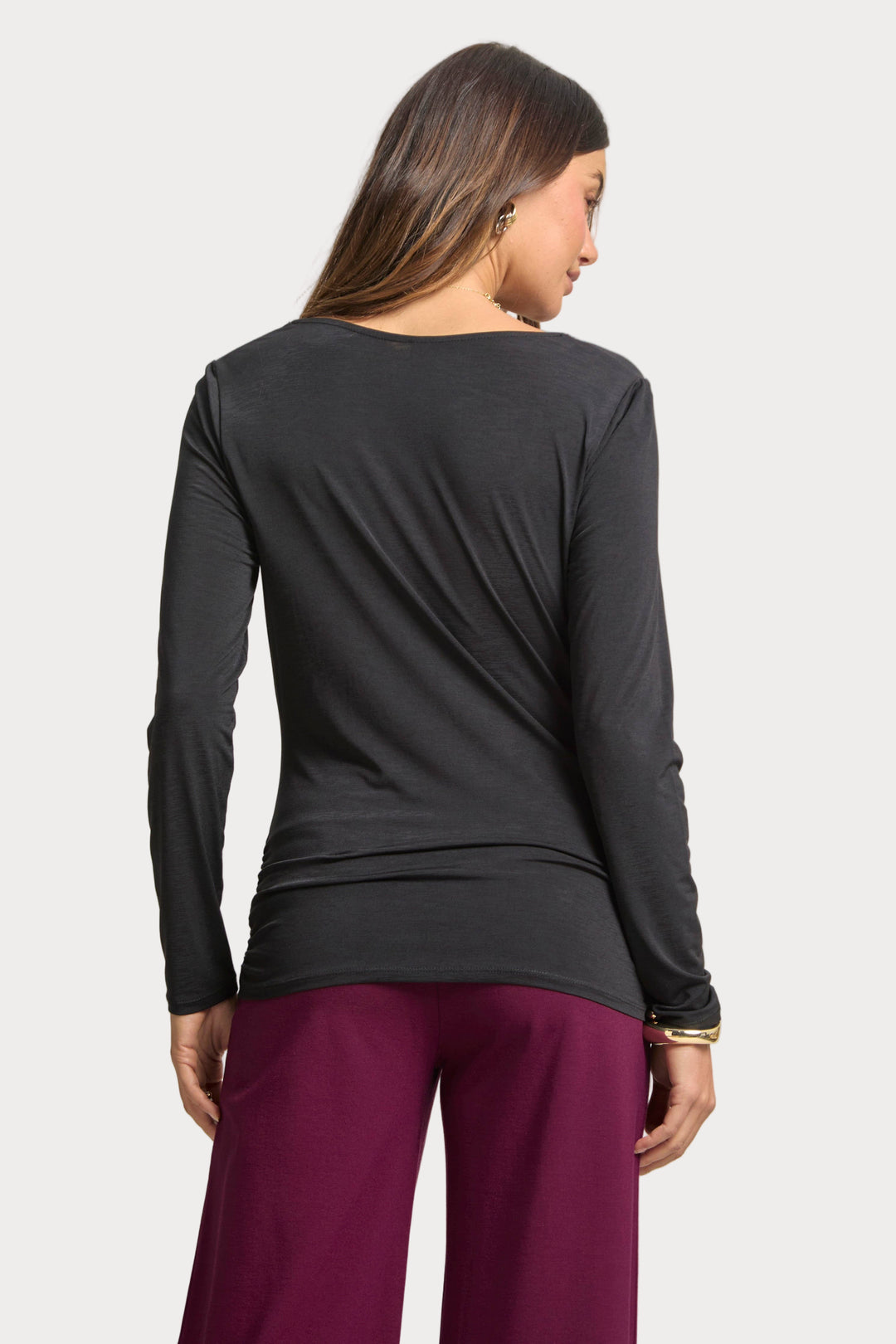 Woman wearing a black long-sleeve top and purple pants on a plain background