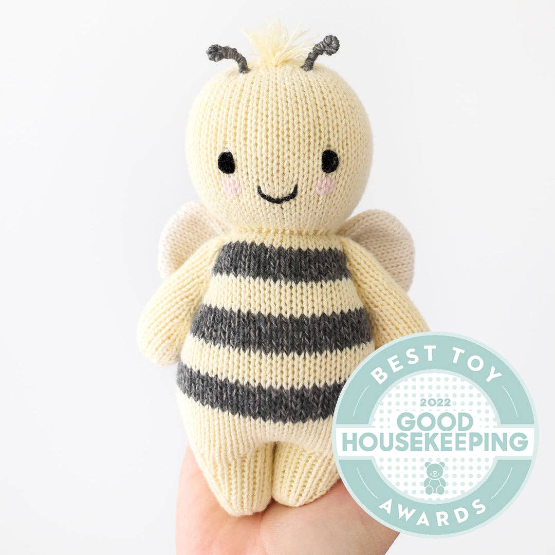 Knitted bee toy held by a hand with Good Housekeeping Award badge.