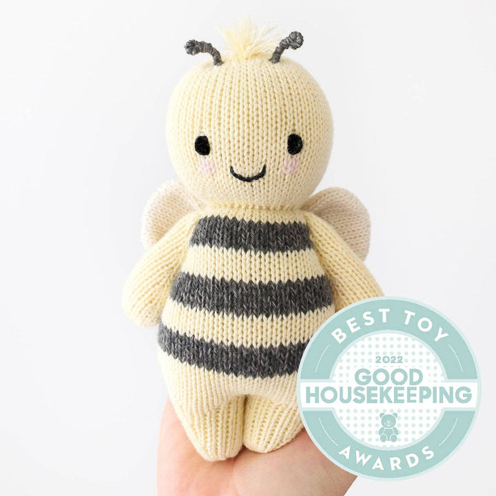 Knitted bee toy held by a hand with Good Housekeeping Award badge.