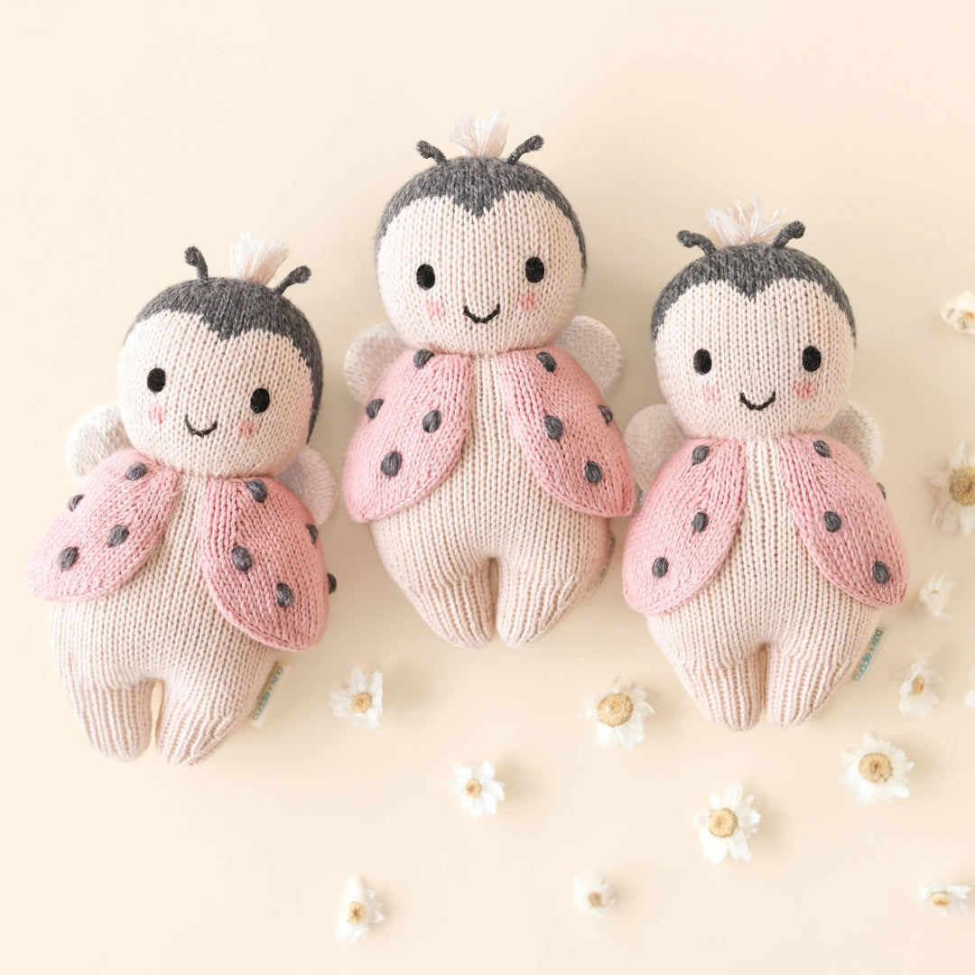 Three knitted ladybug toys on a light background with small flowers.