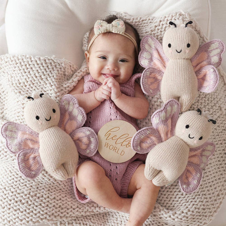 Baby surrounded by knitted butterfly toys with 'hello world' sign on a soft surface