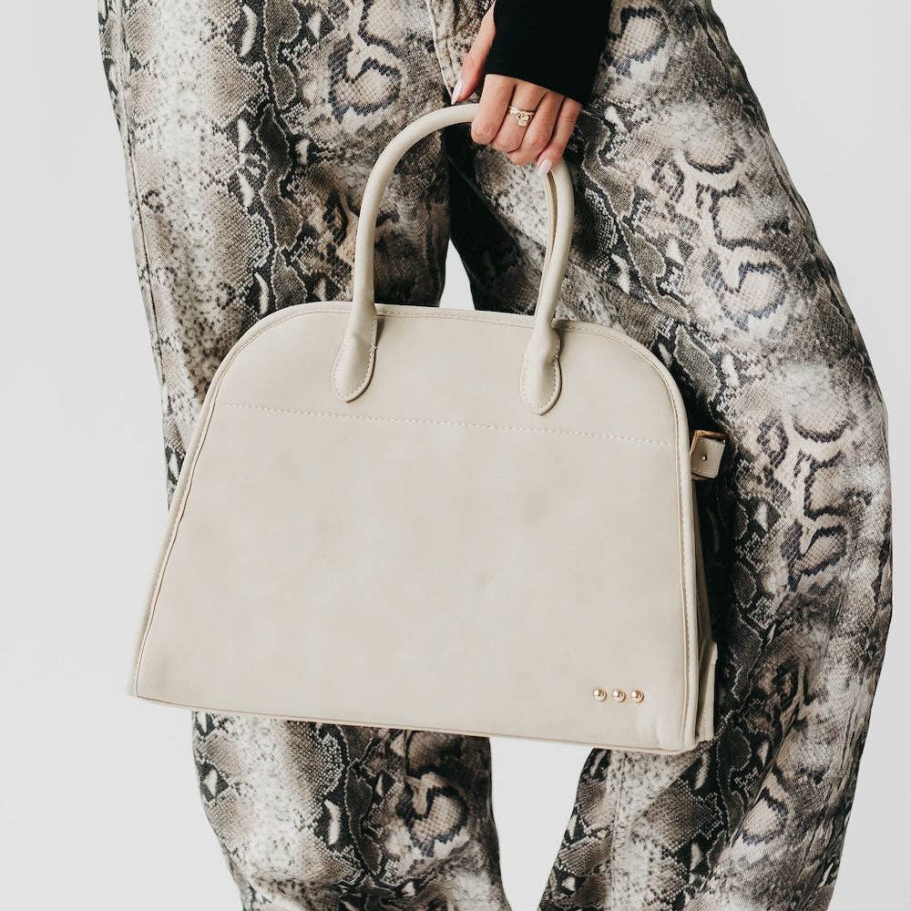 Oat colored handbag held by a person wearing patterned pants on a light background