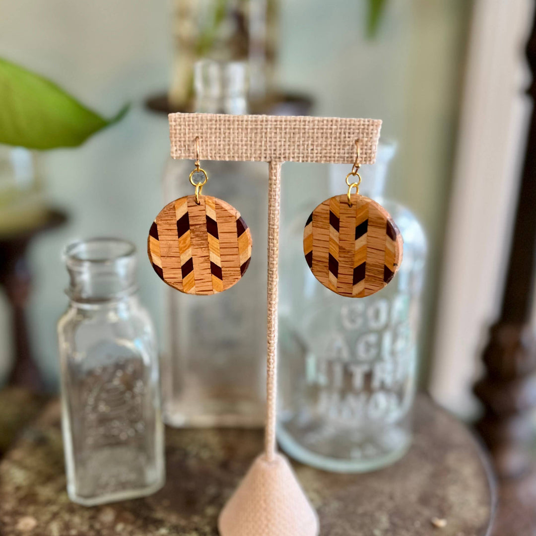 Handcrafted wood laminate circle earrings featuring geometric natural wood patterns and hypoallergenic stainless-steel hardware displayed on an earring stand. 