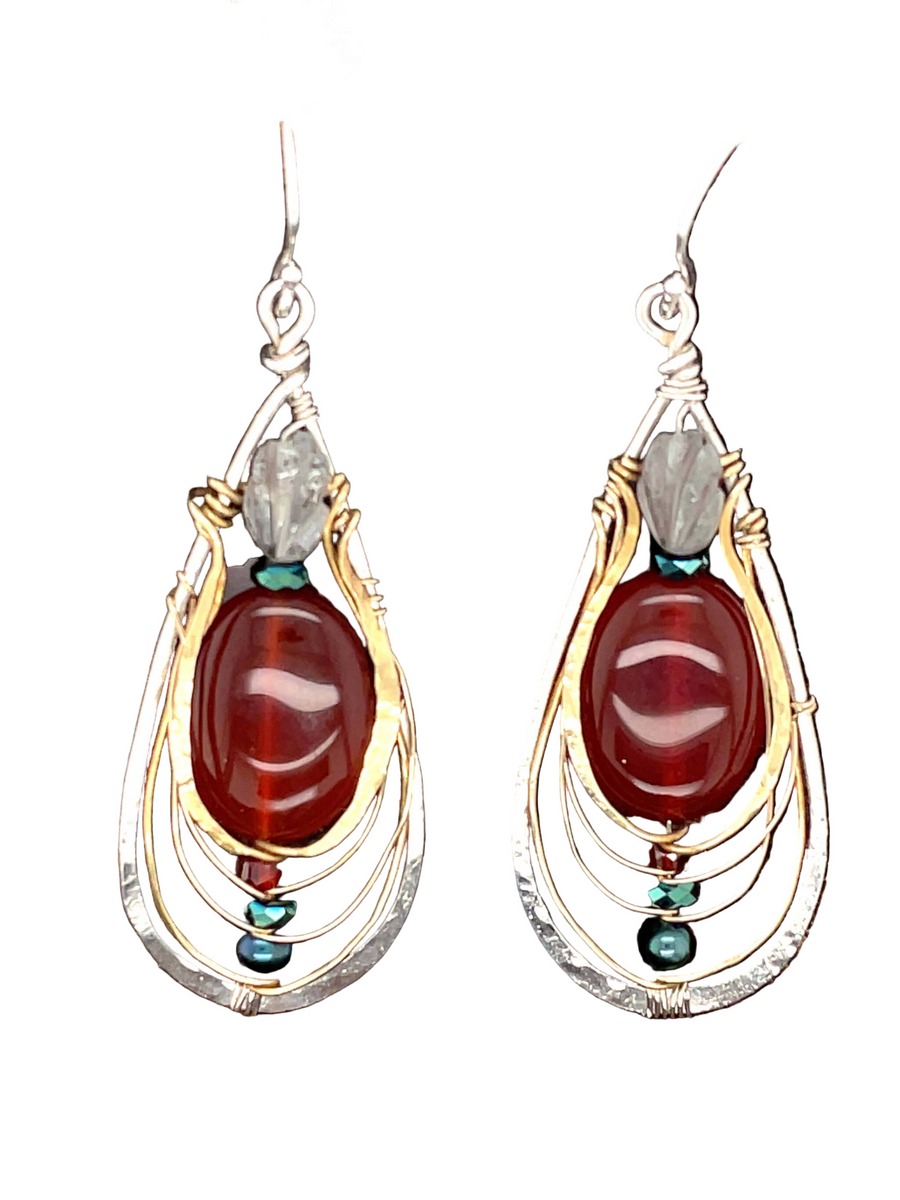 Pair of earrings with carnelian stones  crowned with elegantly carved aquamarine and gold and silver wirework on a white background 