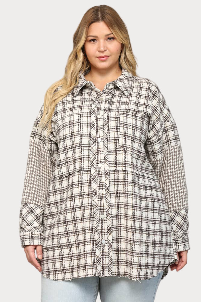 Plus-size model wearing a cream and brown plaid shacket with contrasting houndstooth pattern sleeves. The shirt-jacket is styled, showcasing its relaxed, oversized fit.
