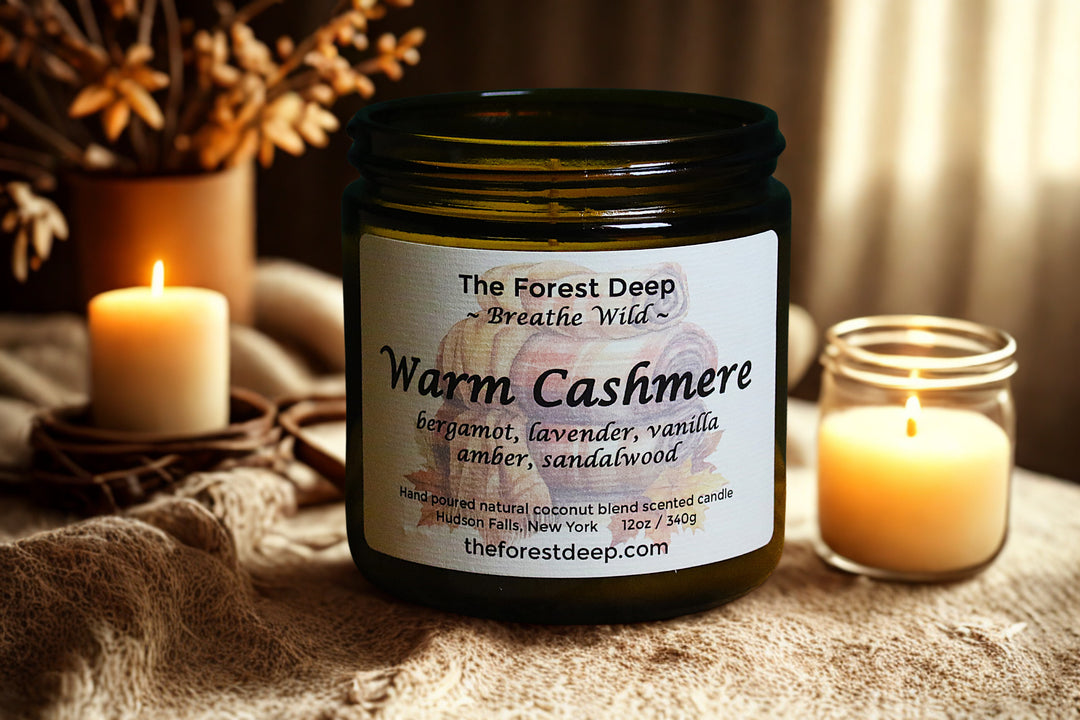 Jar of 'Warm Cashmere' candle with label, surrounded by candles and dried plants on a textured surface.