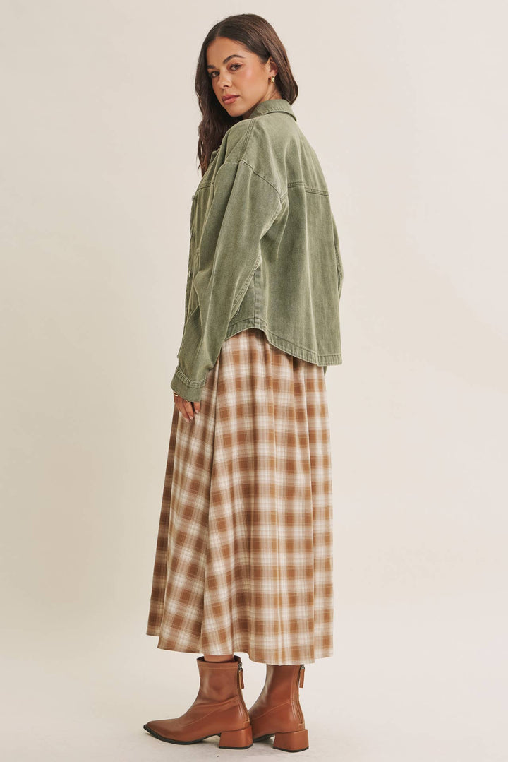 Woman wearing a olive green jacket over a plaid dress on a beige background