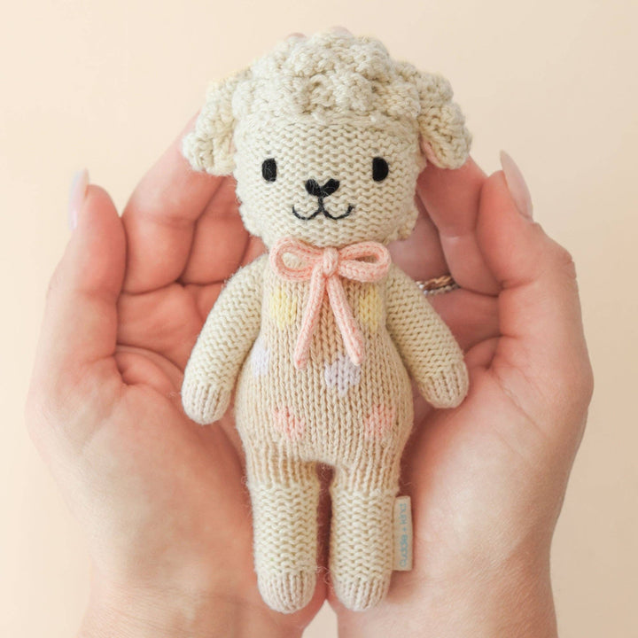 Knitted lamb with a pink bow held in hands against a beige background