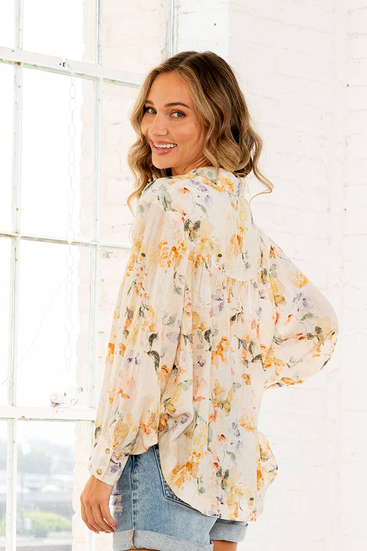 Woman wearing cream watercolor floral button-down blouse with long sleeves and denim shorts