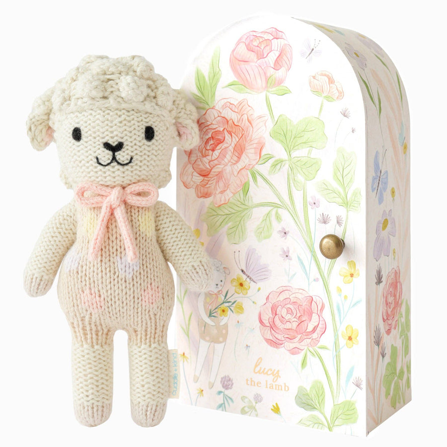 Knitted lamb toy with a floral-patterned box on a beige background