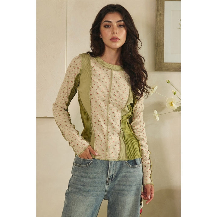 Woman wearing a green and beige patterned top with blue jeans indoors.