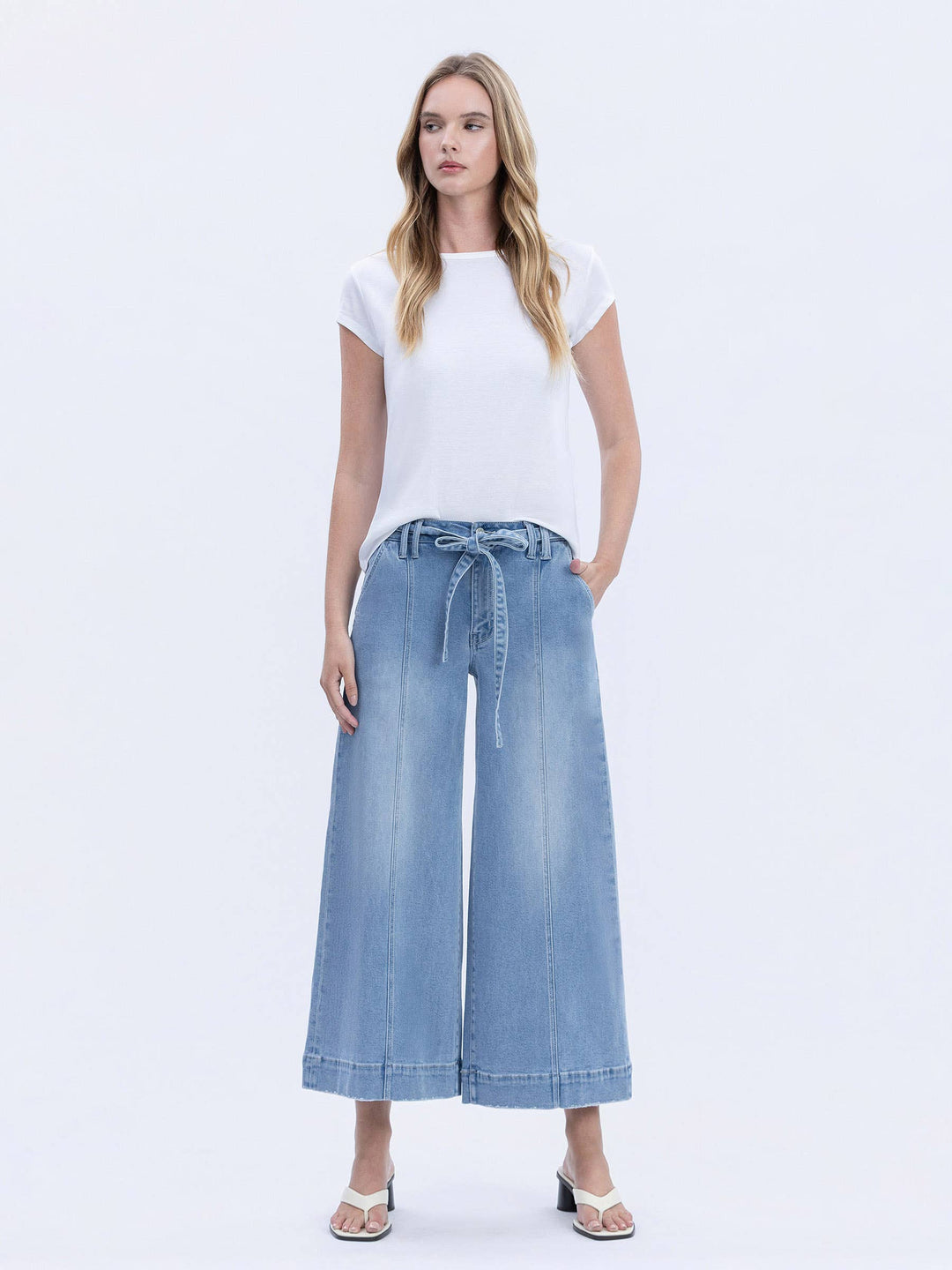 Woman wearing a white t-shirt and blue denim wide-leg pants on a white background