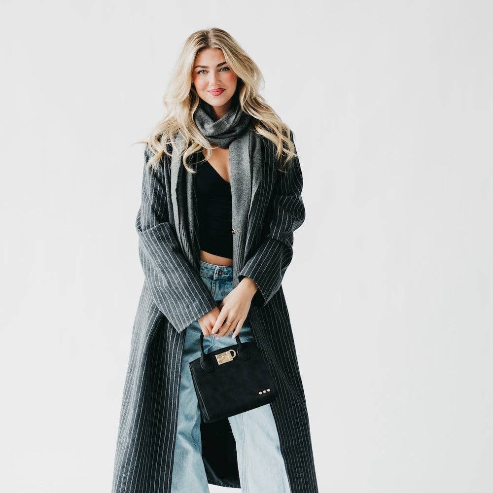 Woman wearing a long gray coat with a black scarf and holding a black handbag on a white background