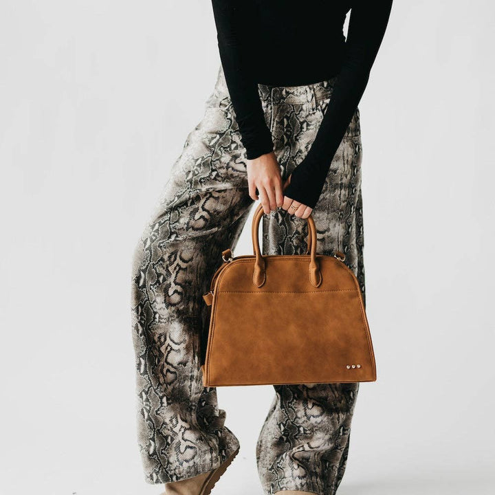 Model holding a camel nubuck vegan leather tote bag with a structured silhouette.