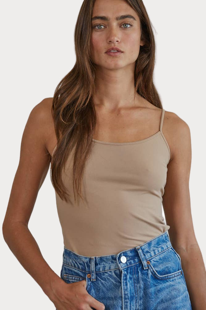 A woman wearing a beige full-length cami tank top and blue denim shorts.