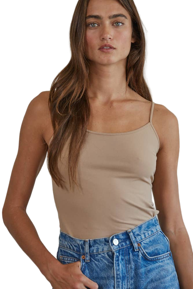 A woman wearing a beige full-length cami tank top and blue denim shorts.