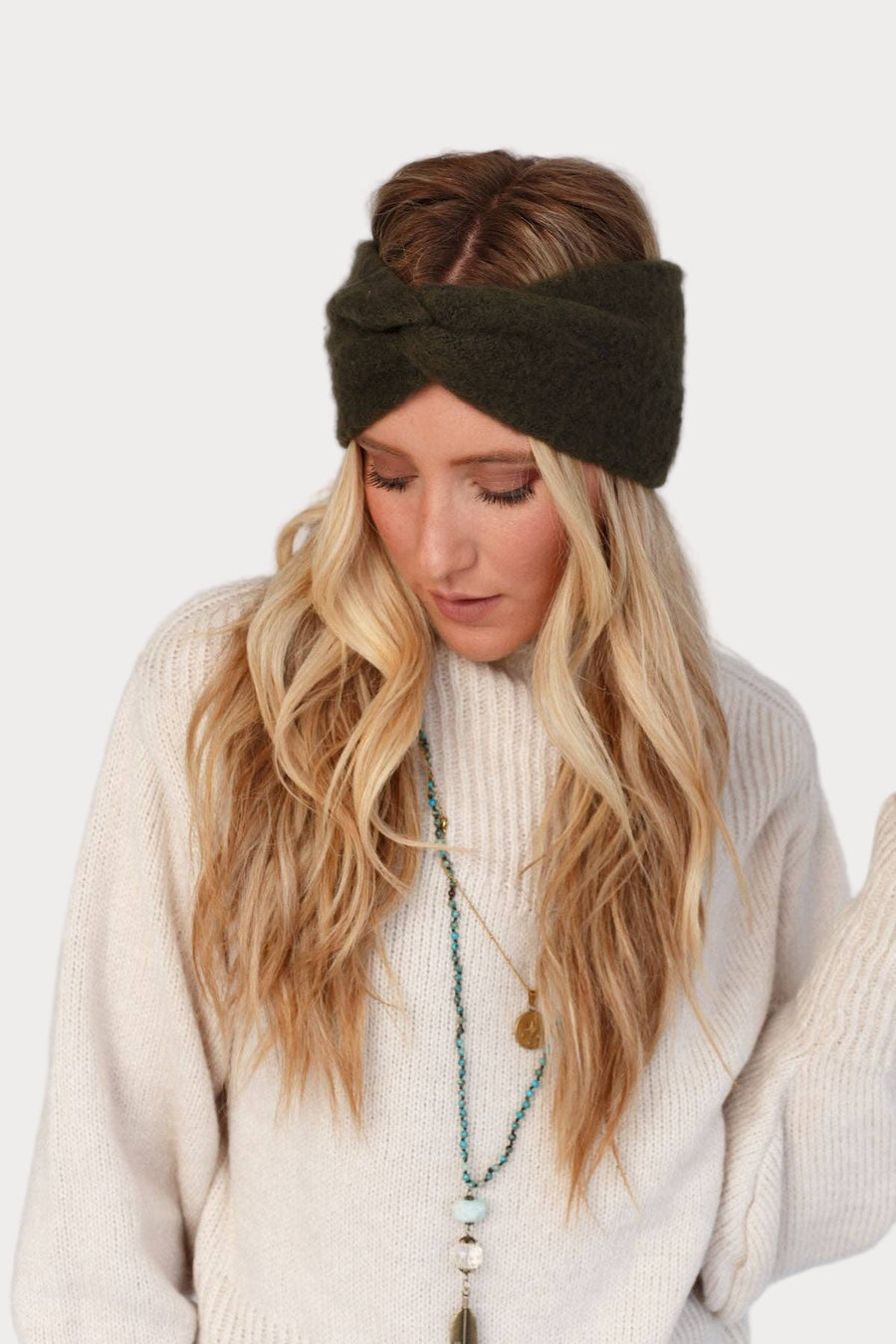 Woman wearing a dark green knitted headband against a white background