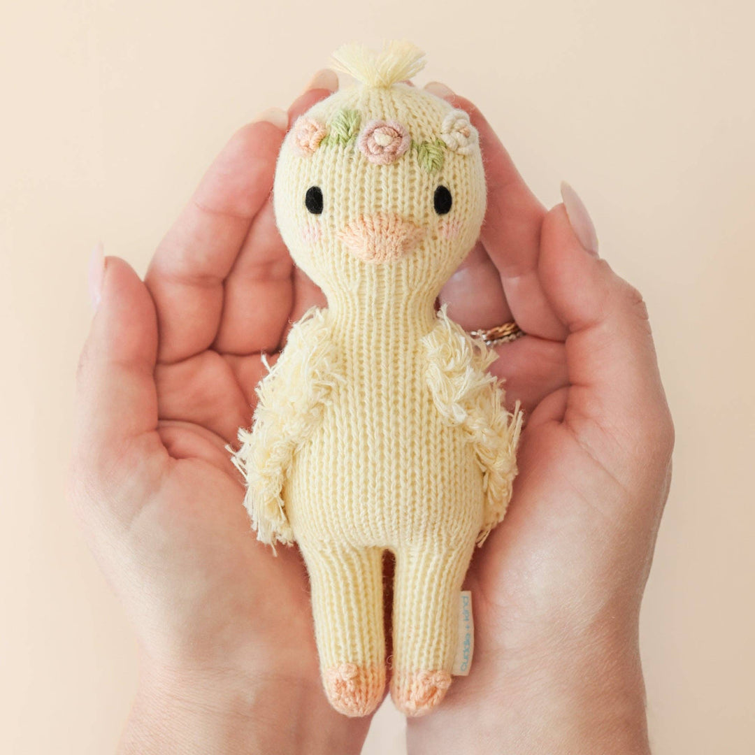 Hand holding a small knitted duckling toy with a plain background