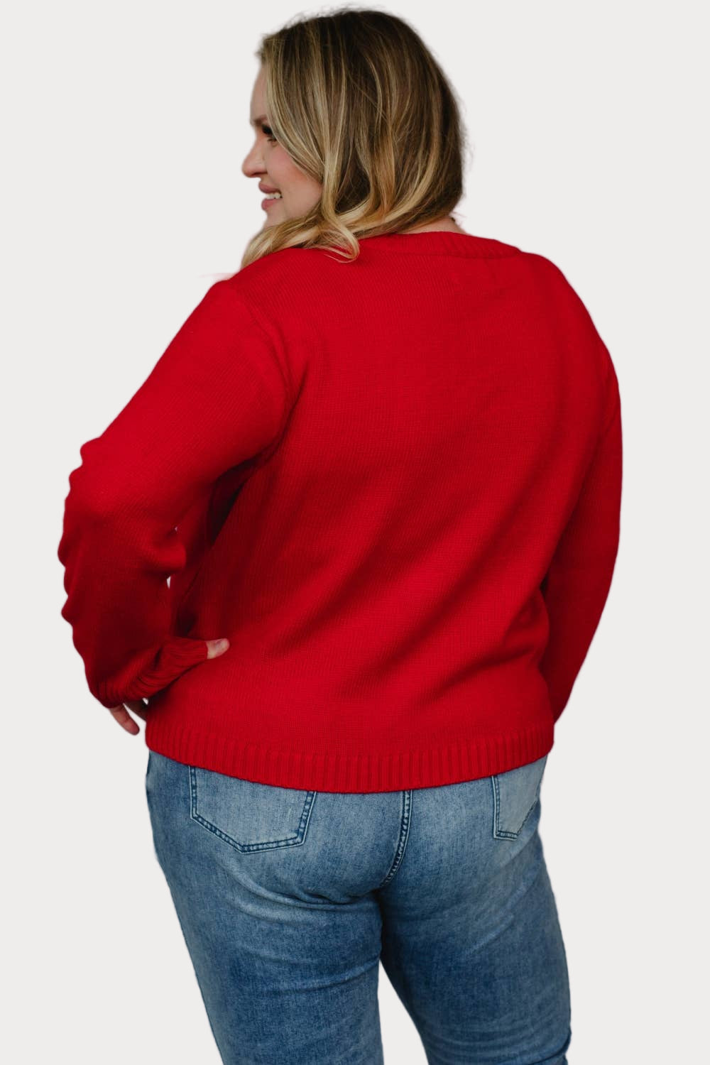 Plus size model wearing a red sweater with 'merry' text against a neutral background view from back