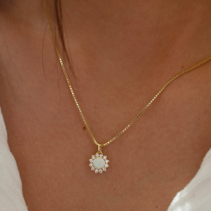 gold necklace with opal center stone and cubic zirconia halo pendant on box chain worn by model