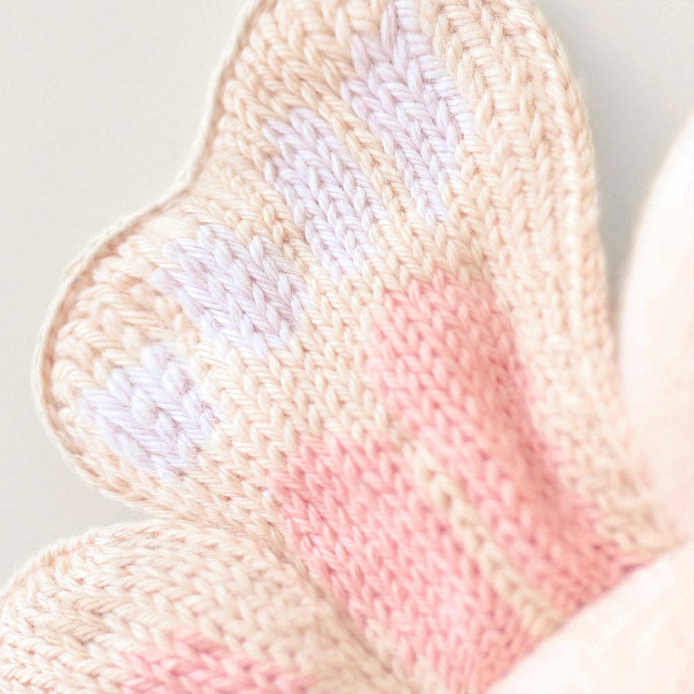 Close-up of a knitted butterfly wing with pink and beige colors on a light background