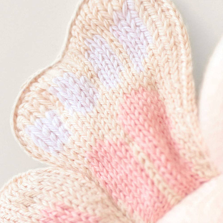 Close-up of a knitted butterfly wing with pink and beige colors on a light background