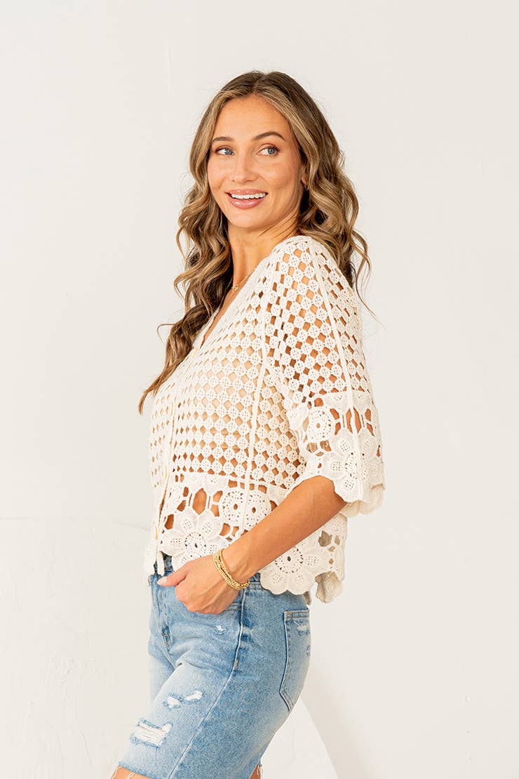 Woman wearing cream crochet button-down top with scalloped lace hem and distressed denim shorts