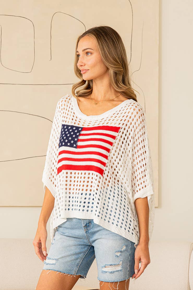 Woman wearing white open-knit sweater top with American flag design and denim jeans