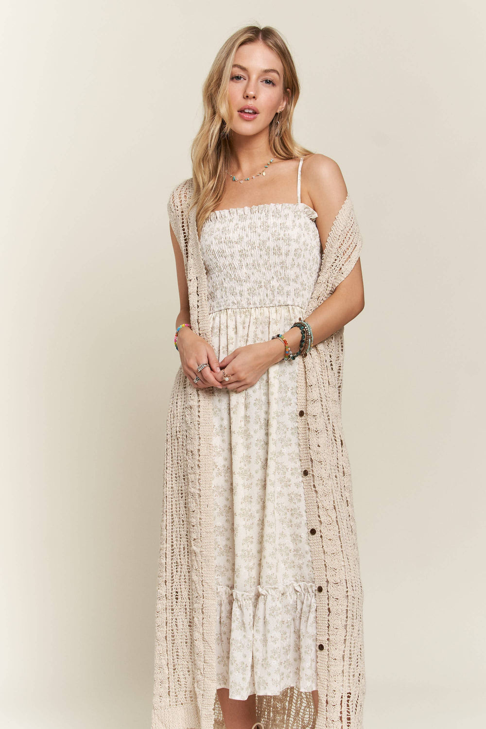 Woman wearing long beige crochet duster vest over a white floral dress