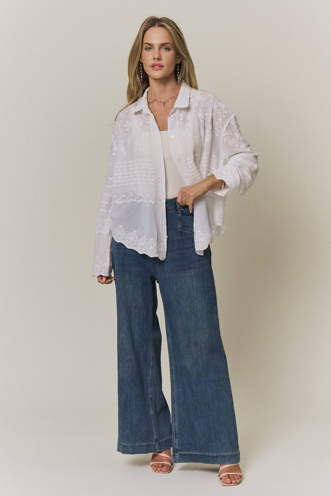 Woman wearing a light-colored lace embroidered blouse and blue jeans against a plain background