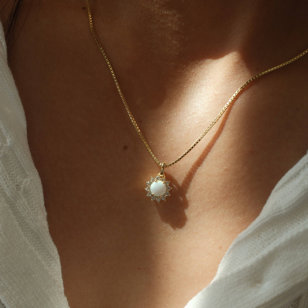 gold necklace with opal center stone and cubic zirconia halo pendant on box chain worn by model