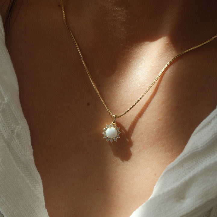 gold necklace with opal center stone and cubic zirconia halo pendant on box chain worn by model
