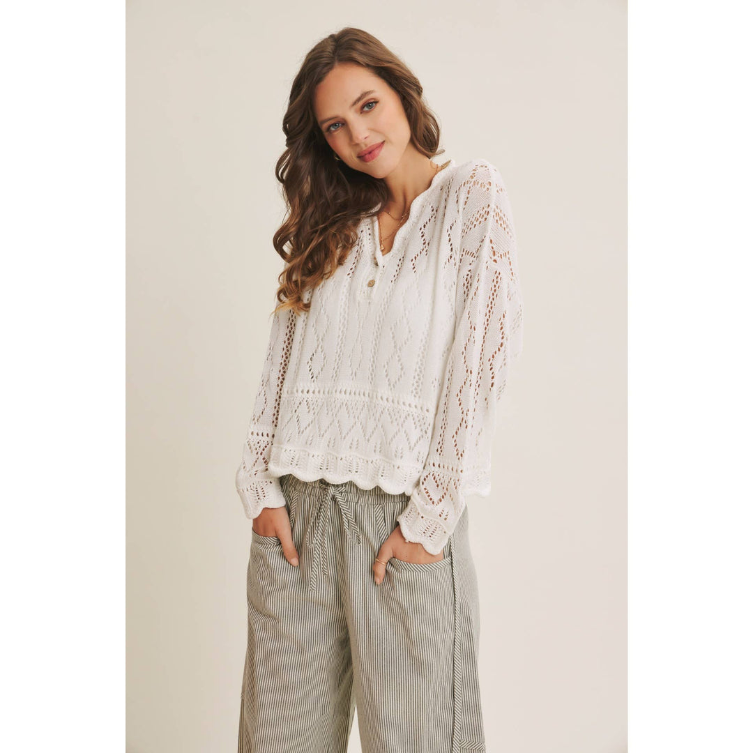 Woman wearing a white open-knit crochet sweater top with scalloped hem and long sleeves