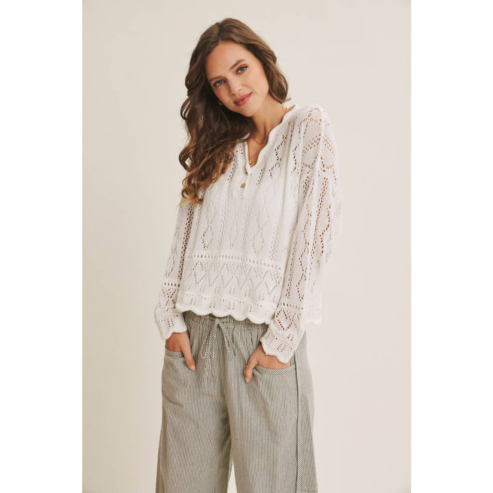 Woman wearing a white open-knit crochet sweater top with scalloped hem and long sleeves