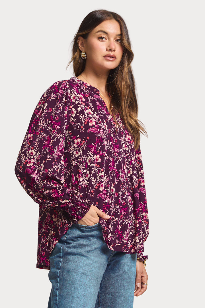 Woman wearing a purple floral blouse and blue jeans on a white background