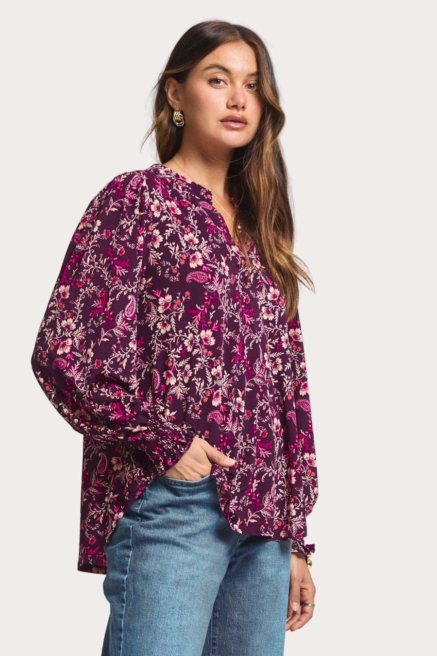 Woman wearing a purple floral blouse and blue jeans on a white background